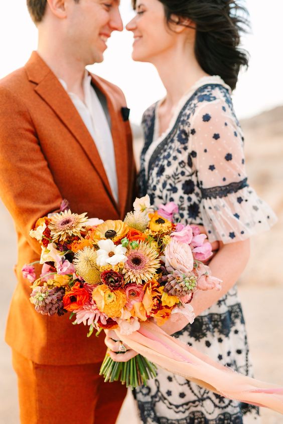 a colorful wedding bouquet of yellow ranunculus and gerberas, pink blooms and red ones and some textural fillers