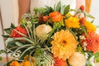 a colorful wedding bouquet of yellow, red and burnt orange roses, ranunculus and dahlias, greenery and air plants