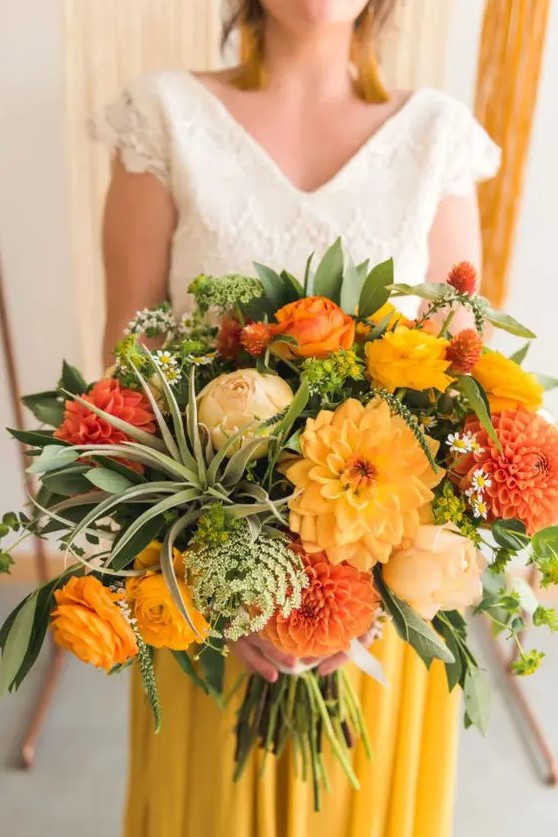 a colorful wedding bouquet of yellow, red and burnt orange roses, ranunculus and dahlias, greenery and air plants