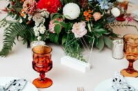 a colorful wedding centerpiece of red, burgundy and white dahlias, orange gerberas, blue blooms, berries and leaves