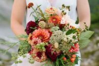 a creative fall wedding bouquet of orange and pink dahlias, burgundy ones, some seed pods and wildflowers, greenery and berries