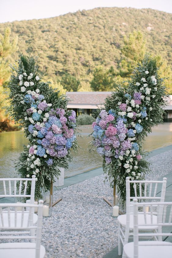 a creative wedding altar shaped as butterfly wings, with greenery, white roses and lilac and blue hydrangeas is a gorgeous idea