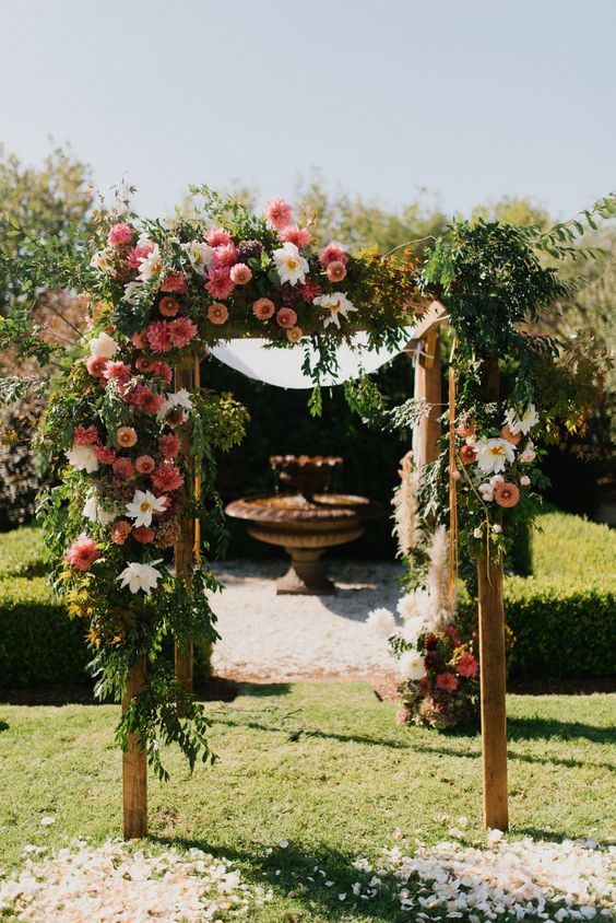 A creative wedding arch done with lush greenery, white, pink and rust colored dahlias looks very eye catching and will match and bold wedding