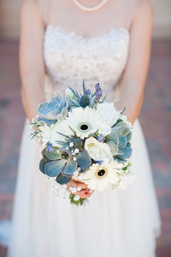 a delicate and stylish wedding bouquet of white gerberas, baby's breath, succulents, thistles and purple touches is chic