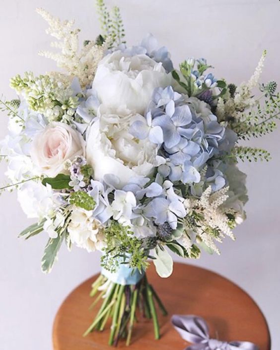 a delicate and textural wedding bouquet of white peonies, blue hydrangeas, blush roses, some fillers and greenery