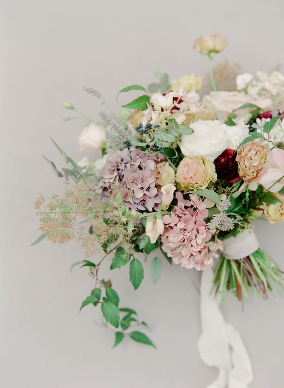 a delicate pastel wedding bouquet of pink hydrangeas, white roses and burgundy ones, some greenery and fillers is a catchy idea for a summer bride