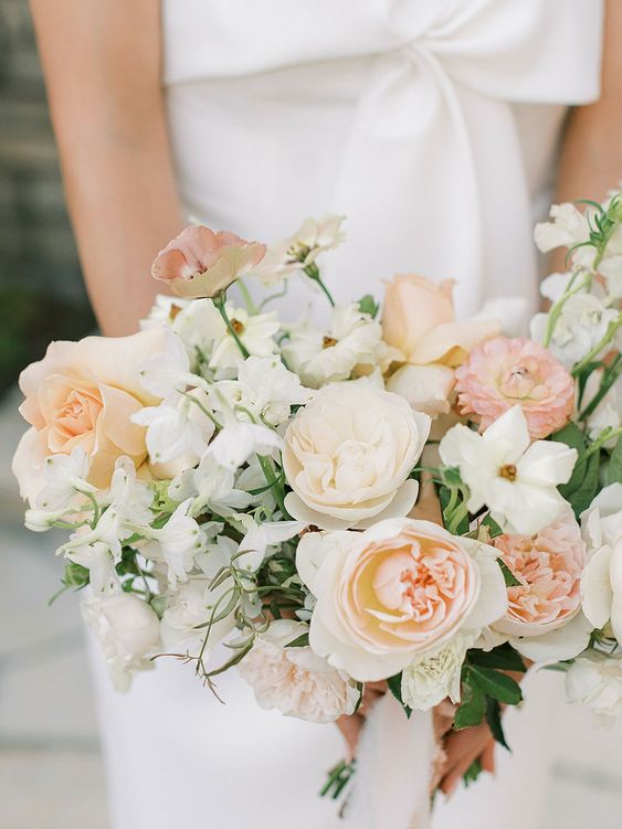 a delicate peach wedding bouquet of white and blush roses and peony roses, carnations and sweet peas blooms