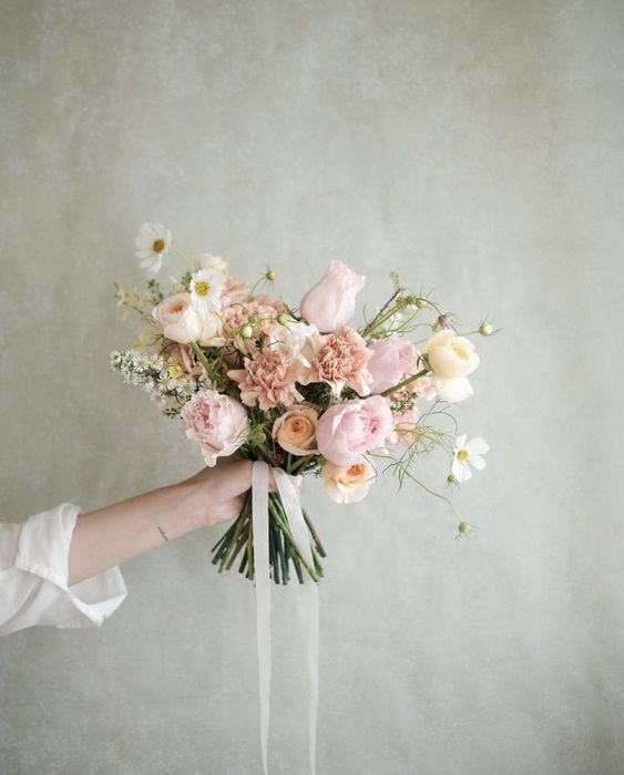 a delicate wedding bouquet of blush and white roses, blush caranations and white fillers, some neutral ribbons is wow