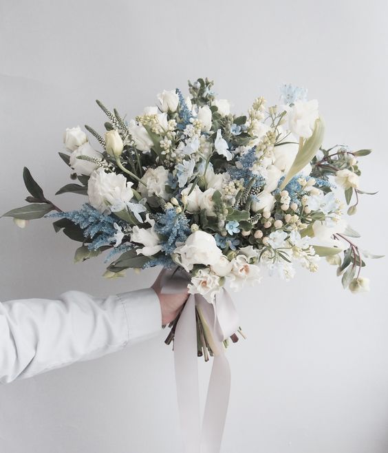 a delicate yet lush wedding bouquet of white tulips, roses and blue fillers, greenery and berries is amazing for a spring or summer wedding
