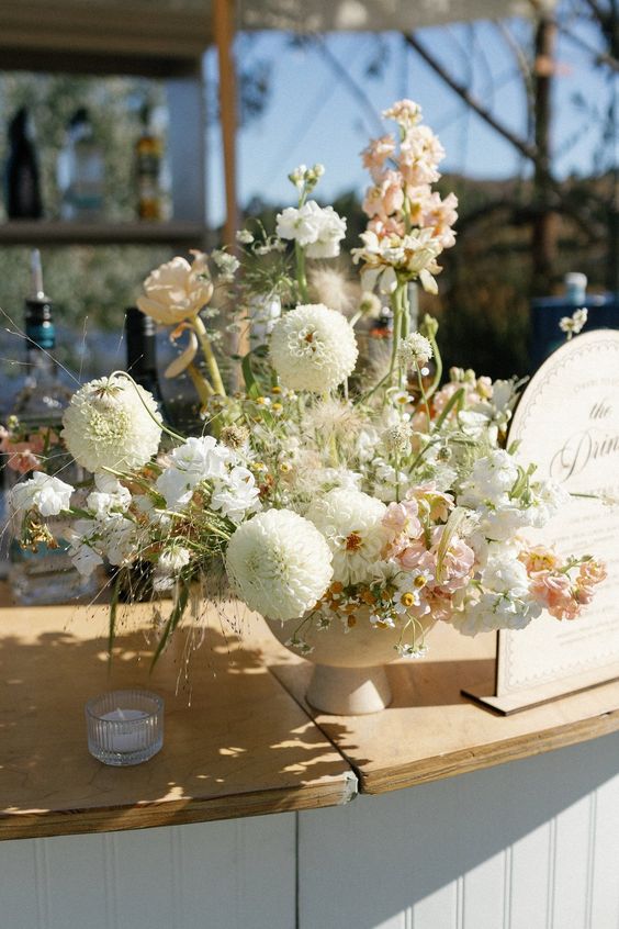 a dimensional wedding centerpiece of white dahlias, blush and white fillers and some greenery for a spring wedding