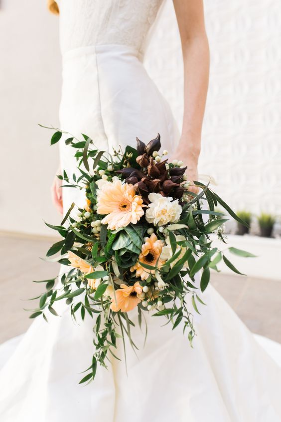 a dramatic wedding bouquet of deep purple callas, orange gerberas and lots of greenery and berries is a catchy idea for a fall wedding
