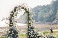 a dreamy coastal wedding arch done with lots of twigs and branches, white roses, blue hdyrangeas and lots of greenery plus a coastal view