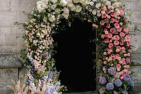 a fab wedding arch over the church entrance made of blush, white, pink, purple and lilac blooms, mostly dahlias, roses and hydrangeas and an ombre effect