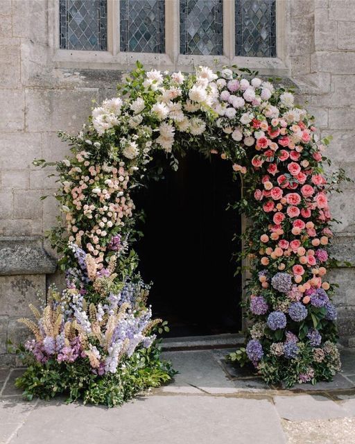a fab wedding arch over the church entrance made of blush, white, pink, purple and lilac blooms, mostly dahlias, roses and hydrangeas and an ombre effect