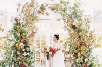 a fabulous and textural fall wedding arch with burgundy, pink and yellow blooms, greenery and fall foliage is amazing for an autumn celebration