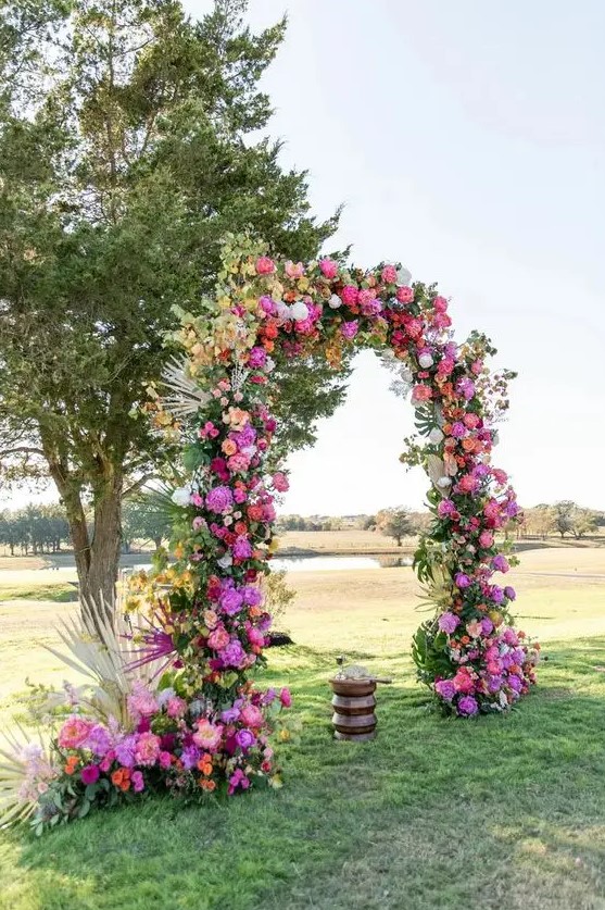 a fabulous wedding arch with peachy, orange and hot pink blooms, greenery and frinds is a lovely idea for a bright wedding