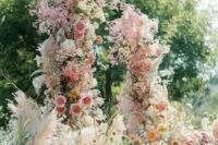 a fantastic and super lush wedding arch with pink, yellow and orange blooms and blooming branches plus pink baby’s breath all over