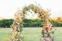 a fantastic bright wedding arch with yellow, pink, blue and lilac blooms and greenery is amazing for a bright wedding