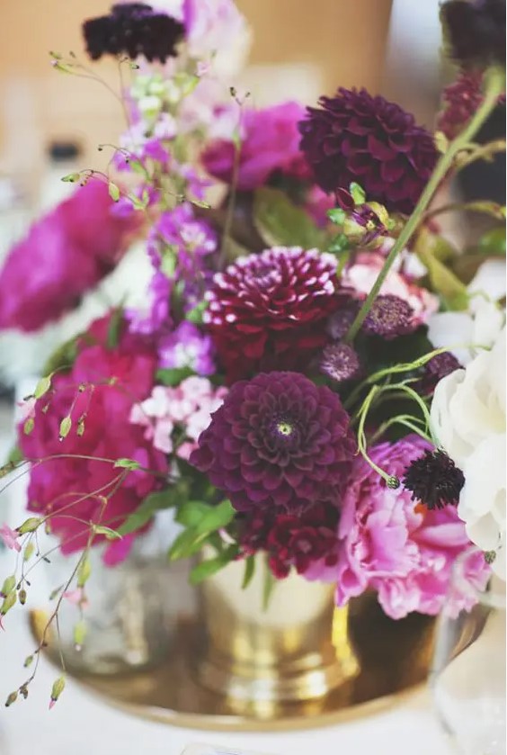 a fantastic jewel tone wedding centerpiece with pink, creamy, deep purple and hot pink blooms and greenery in gold vases