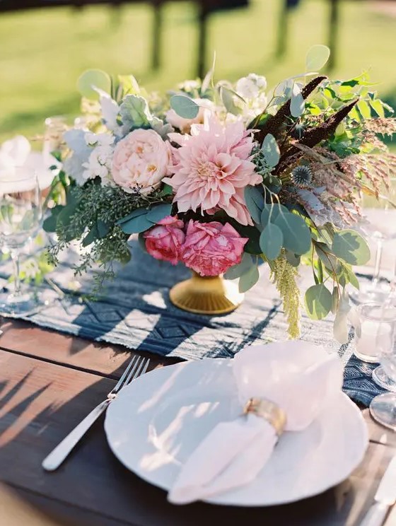 a fantastic wedding centerpiece of pink dahlias, peony roses, greenery, allium and feathers for a summer wedding