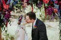 a gorgeous bold wedding arch with blue, purple, burgundy, hot red and lilac blooms and greenery for the fall