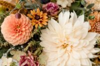 a gorgeous fall wedding centerpiece of white and peachy dahlias, pink, yellow and neutral fillers, greenery and figs