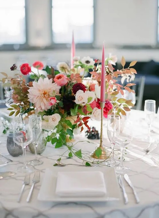 a gorgeous fall wedding centerpiece of white roses, pink ranunculus, blush and burgundy dahlias, greenery and fall leaves