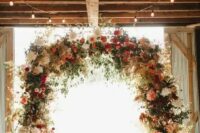 a gorgeous rustic fall wedding arch done with lots of greenery, pampas grass, blush, deep red, burgundy dahlias and candle lanterns