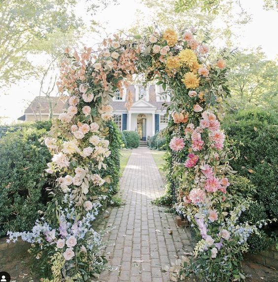 a gradient wedding arch done with blue, lilac, blush and pink, yellow and bold pink dahlias and other blooms plus greenery