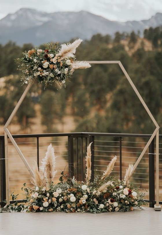 a hexagon wedding arch with a flower and pampas grass arrangement on one corner and a floral arrangement at the base is amazing