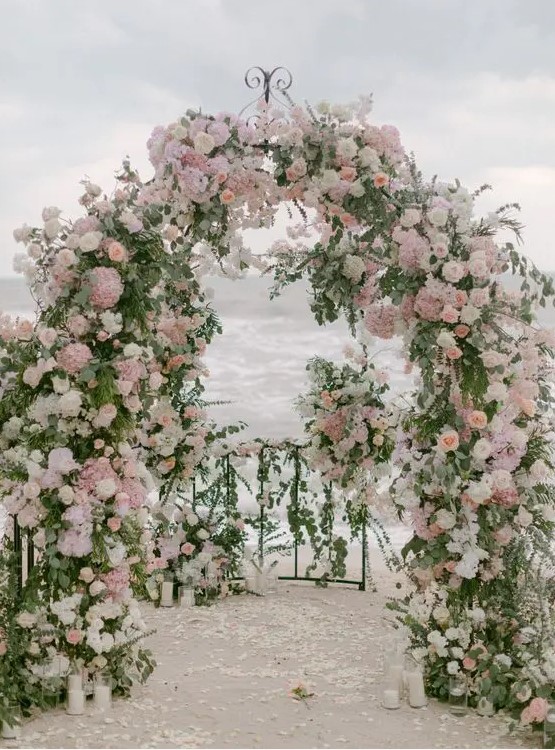 A jaw dropping beach garden wedding arch decorated with greenery, white, blush and mauve blooms is just jaw dropping and chic