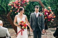 a lovely hexagon wedding arch decorated with pink peonies, red and blush roses and greenery is a cool idea for a bright modern wedding