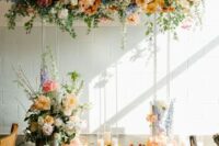a lovely pastel wedding arch with white, orange, rust, blue and pink blooms, blooming branches and greenery and candles on the floor for a spring wedding