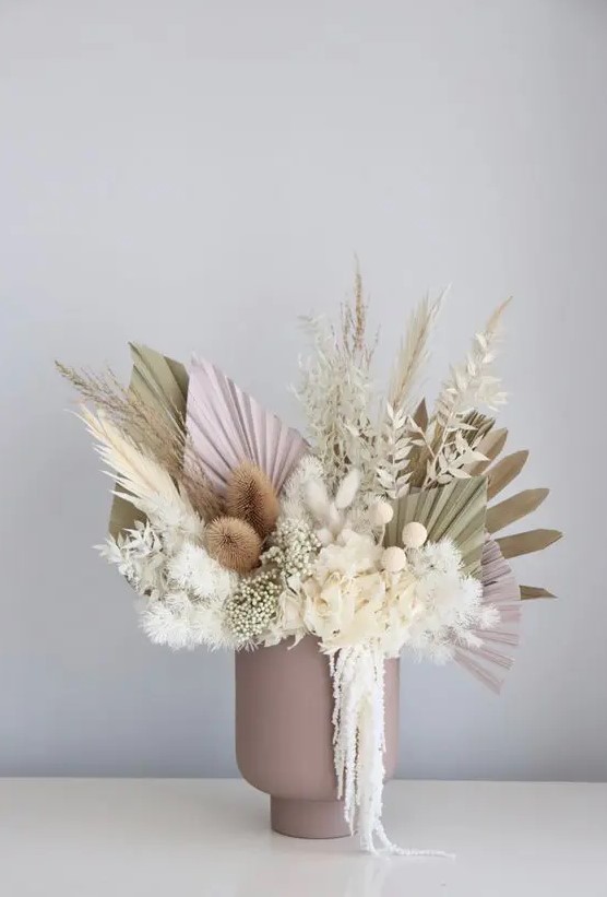 a lovely pastel wedding centerpiece in a dusty pink vase, with neutral and pink fronds, grasses, billy balls, dried white leaves is cool