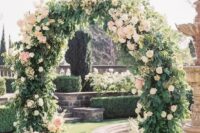 a lovely round wedding arch covered with greenery and with some blush flowers here and there is a very chic and elegant idea for a garden wedding