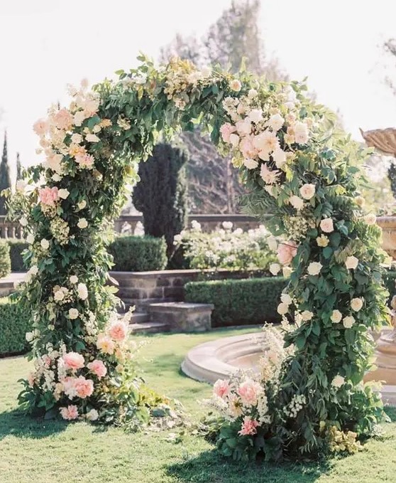 a lovely round wedding arch covered with greenery and with some blush flowers here and there is a very chic and elegant idea for a garden wedding