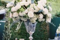 a lovely tall wedding centerpiece of a crystal vase, white blooms and lots of greenery and eucalyptus is a chic idea