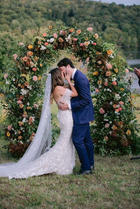 a lovely wedding arch decorated with greenery, white, blush, mustard and rust-colored dajlias and roses looks delicate