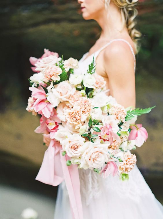 a lovely wedding bouquet of blush and pink roses and carnations, orchids and some fern, long pink ribbon