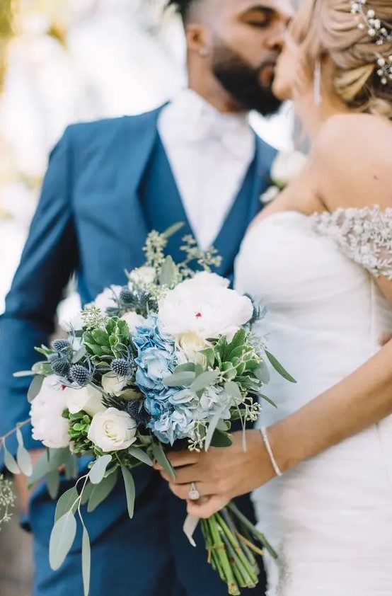 a lovely wedding bouquet of white roses, blue hydrangeas, thistles and greenery is a chic idea for spring or summer