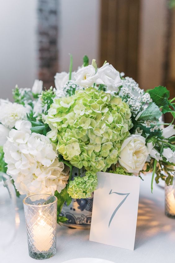 a lovely wedding centerpiece of green and white hydrangeas, white roses and candles is a cool idea for spring and summer