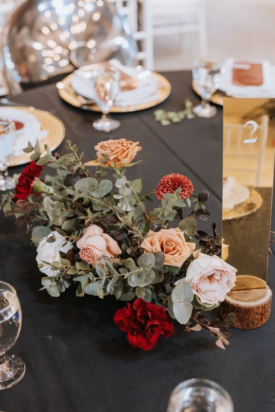 a lovely wedding centerpiece of greenery, blush and rust roses, red carnations and blush peony roses plus greenery