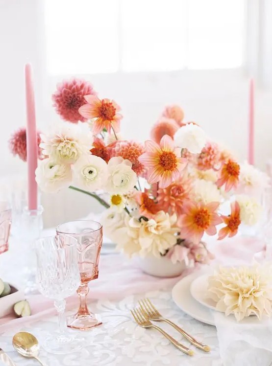 a lovely wedding centerpiece of pink and orange dahlias, white ranunculus and dahlias and some pink candles