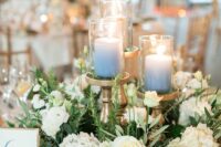 a lovely wreath wedding centerpiece of white hydrangeas and roses, some greenery and ombre blue candles on tall stands