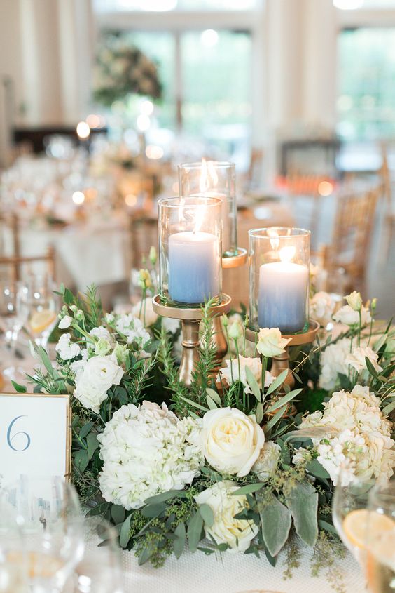 a lovely wreath wedding centerpiece of white hydrangeas and roses, some greenery and ombre blue candles on tall stands
