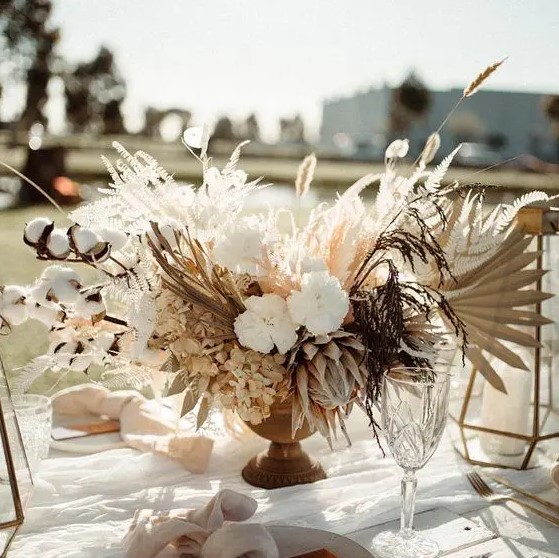 a lush and lovely wedding centerpiece of white fresh and dried blooms, fronds, grasses, cotton and bunny tails is a pretty idea