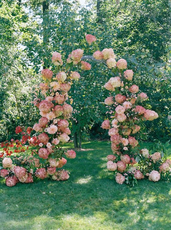 a lush pink wedding arch with greenery and some pink hydrangeas and dahlias is a gorgeous idea for a spring or summer wedding