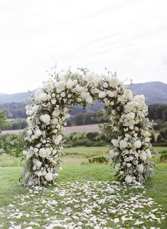 a lush wedding arch covered with greenery and white hydrangeas is a classic idea for any wedding, add petals to the ground