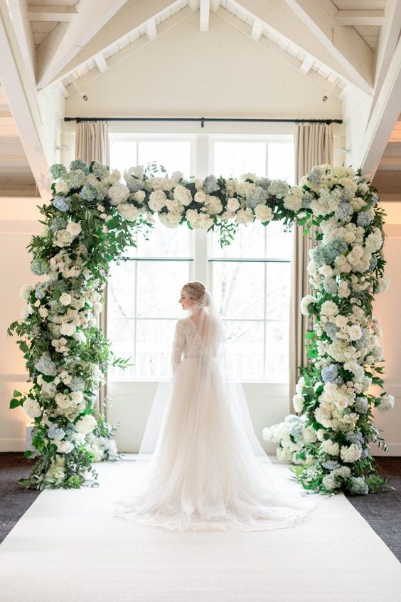 a lush wedding arch decorated with white and blue hydrangeas and greenery is an elegant and traditional idea for spring and summer