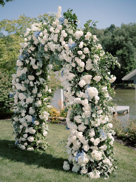 a lush wedding arch with greenery and lots of white hydrangeas plus some blue touches is a cool and chic idea to rock